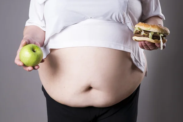 Les femmes souffrent d'obésité avec un grand hamburger et pomme dans les mains. Concept de malbouffe — Photo