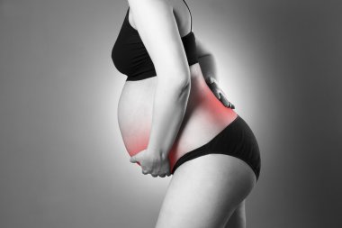 Caucasian pregnant woman in black lingerie with back and abdominal pain on gray studio background clipart