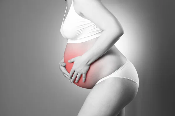 Kaukasische zwangere vrouw in witte lingerie met buikpijn op grijze studio achtergrond — Stockfoto