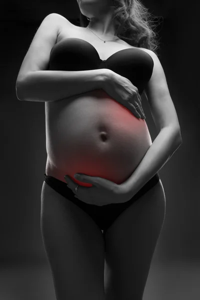 Mujer embarazada caucásica en lencería negra con dolor abdominal sobre fondo gris estudio —  Fotos de Stock