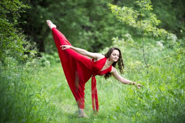 Güzel genç Kafkas esmer kadın kırmızı elbise açık havada, esneklik ve doğa üzerinde uzanan