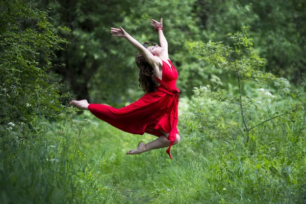 Happy beautiful young caucasian brunette woman in red dress jumping outdoors — Stock Photo, Image