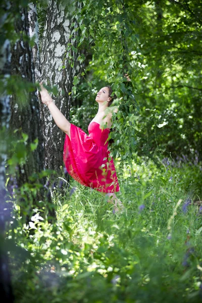 Hermosa joven caucásica morena mujer en vestido rojo al aire libre, flexibilidad y estiramiento en la naturaleza —  Fotos de Stock