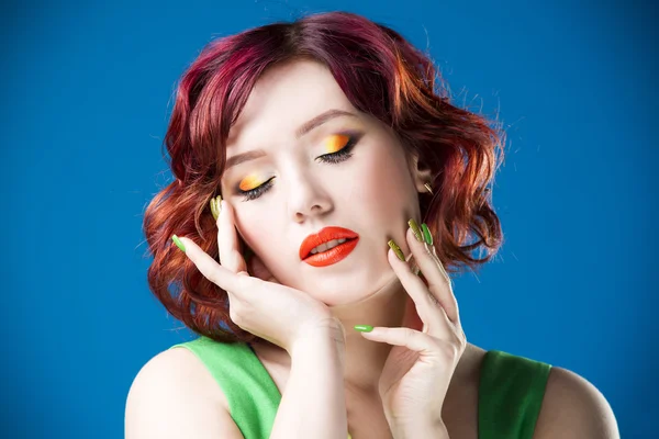 Young beautiful red-haired caucasian woman in green dress posing in studio on blue background, professional makeup and hairstyle — Stock Photo, Image