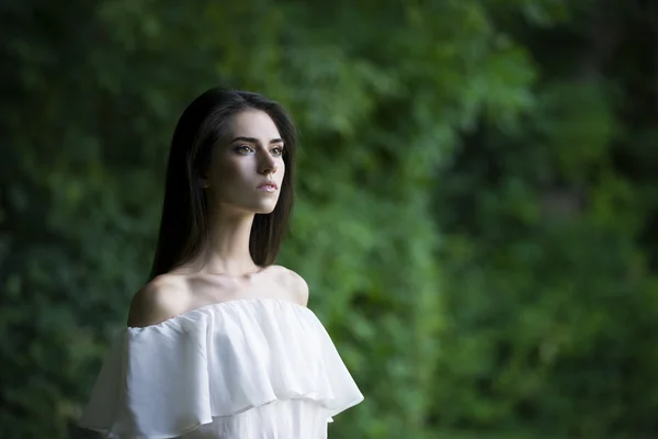 Retrato de uma bela jovem caucasiana de vestido branco com ombros abertos, pele limpa, cabelos longos e maquiagem casual — Fotografia de Stock