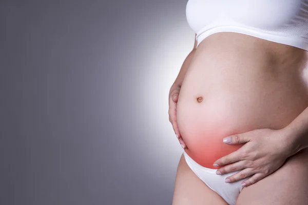 Caucasian pregnant woman in white lingerie with abdominal pain on gray studio background — Stock Photo, Image