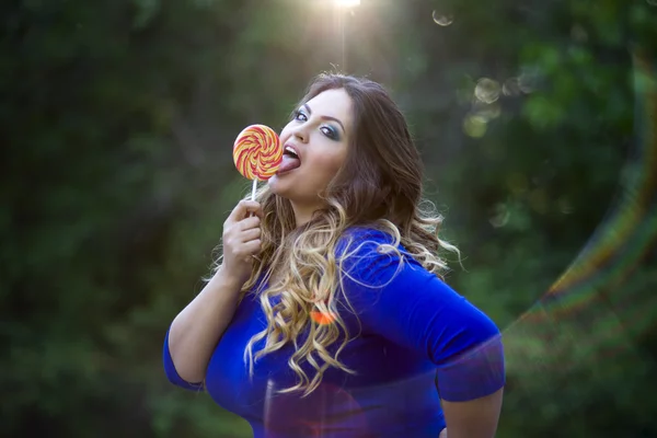 Joven hermosa caucásica más modelo de tamaño en vestido azul al aire libre, xxl mujer en la naturaleza lamiendo una piruleta —  Fotos de Stock