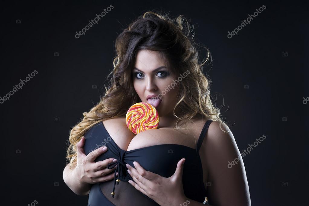 Young beautiful caucasian plus size model with big breast in black bra  licking a lollipop, xxl woman on dark background Stock Photo by ©starast  122542482