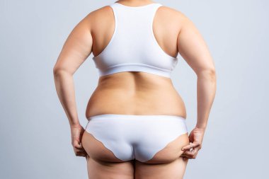 Şişman kalçaları ve kalçaları olan şişman bir kadın, gri arka planda obez bir kadın vücudu, stüdyo çekimi.