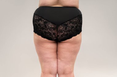 Şişman kalçaları ve kalçaları olan şişman bir kadın, gri arka planda obez bir kadın vücudu, stüdyo çekimi.