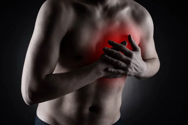 Heart attack, diseases of the cardiovascular system, man with chest pain on black background, painful area highlighted in red