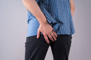 Basur hastası bir adam, gri arka planda anal ağrı, stüdyo çekimi.