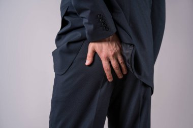 Hemoroitten muzdarip ofis çalışanı, gri arka planda anal ağrı, stüdyo çekimi.