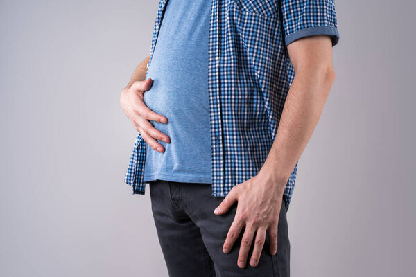 Fat man with bloating and abdominal pain, overweight male body on gray background, studio shot