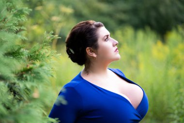 Mavi elbiseli, açık hava yakalı seksi, iri göğüslü, güzel, şişman bir kadın, vücut pozitifliği.