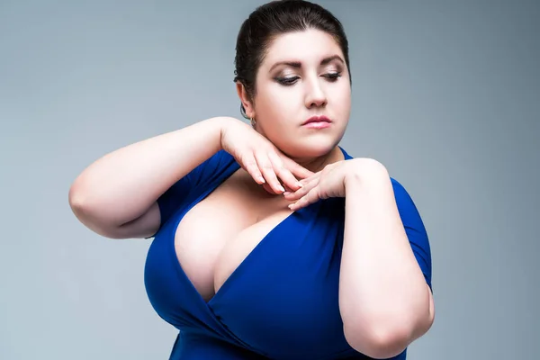 Sexy plus size fashion model in black blouse with deep neckline, fat woman on gray studio background, body positive concept