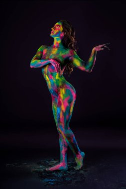 Siyah arka planda parlak renkli vücut sanatı, tozlu boyalarla boyanmış seksi çıplak kadın, stüdyo çekimi.