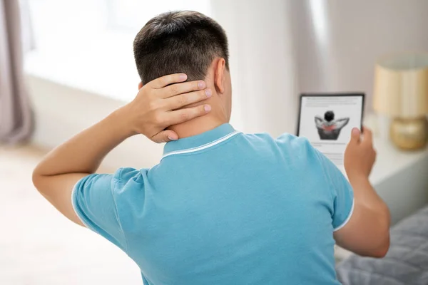 Man with neck pain suffering at home and searches the Internet for symptoms of the disease, online medicine concept