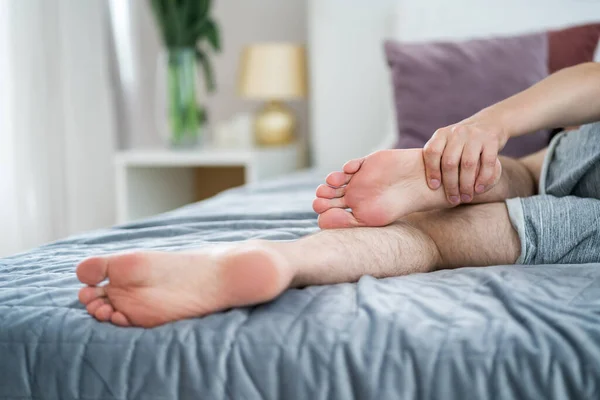 Foot pain, man suffering from feet ache in home interior, podiatry concept