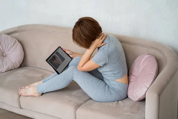 Woman with neck pain suffering at home and searches the Internet for symptoms of the disease, online medicine concept