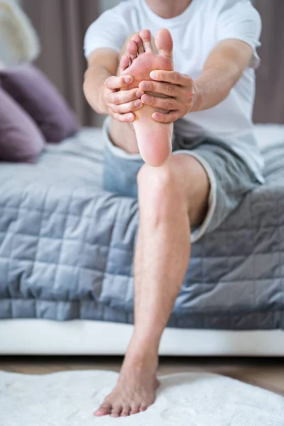 Foot pain, man suffering from feet ache in home interior, podiatry concept