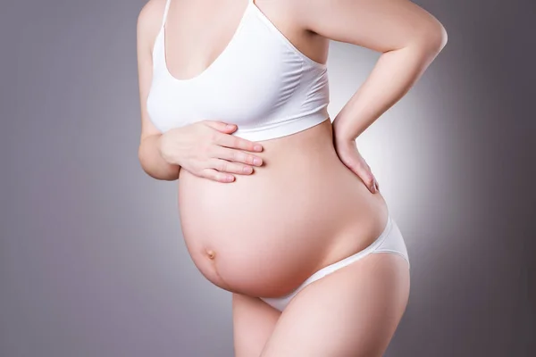 Pregnant woman with back pain, labor pains, risk of premature birth, gray background