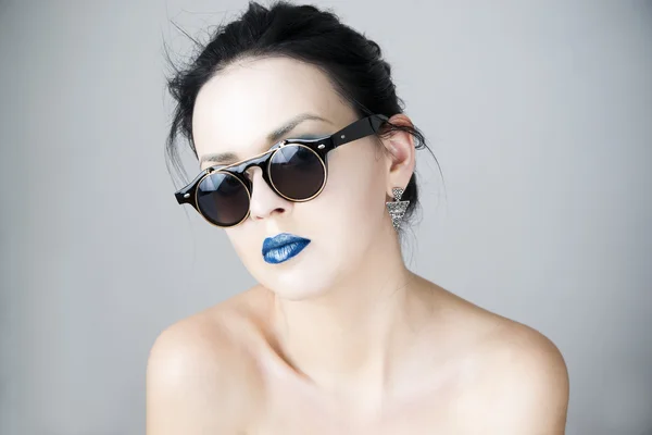 Güzel bir genç kadın güneş gözlüğü gri arka plan üzerinde — Stok fotoğraf