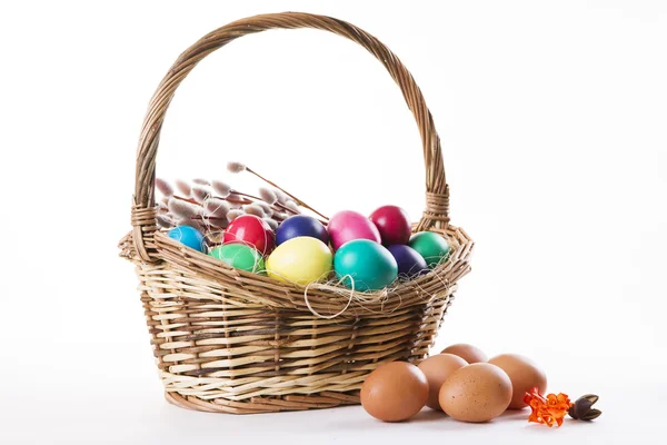 Cesto di vimini con uova colorate e rami di salice su sfondo bianco — Foto Stock