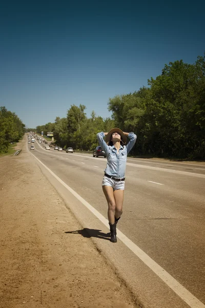 Junge schöne Frau trampt auf einer Straße — Stockfoto