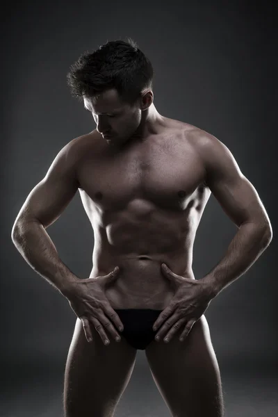 Bonito fisiculturista muscular posando em fundo cinza. Baixo tiro estúdio chave — Fotografia de Stock