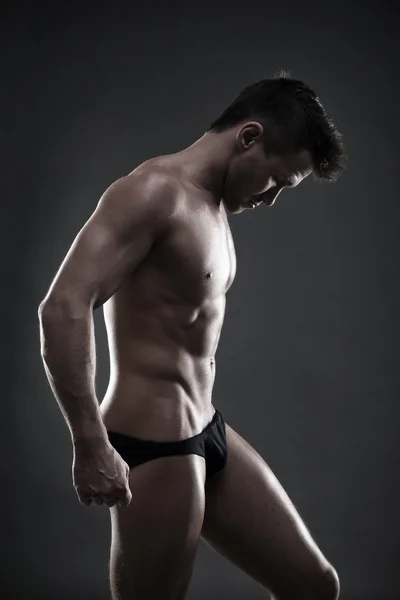Bello bodybuilder muscolare in posa su sfondo grigio. Basso colpo di studio chiave — Foto Stock