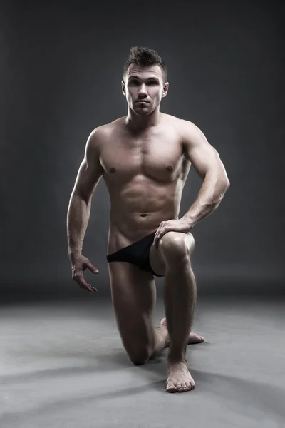 Handsome muscular bodybuilder posing on gray background. Low key studio shot — Stock Photo, Image