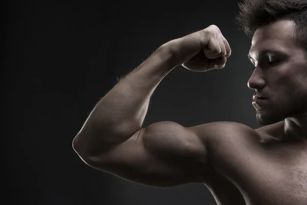 Stilig muskulös bodybuilder poserar på grå bakgrund. Låg nyckel studio skott — Stockfoto