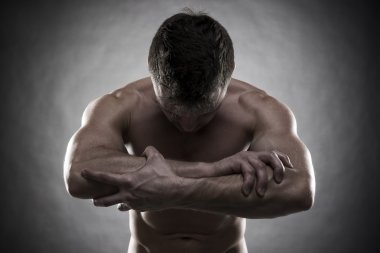 Yakışıklı kaslı vücut geliştirmeci gri arka plan üzerinde poz. Düşük anahtar studio vurdu