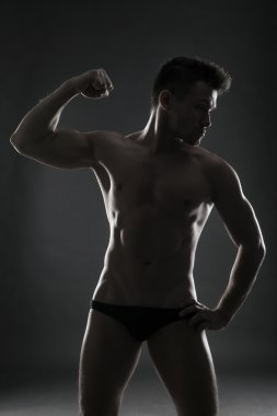 Yakışıklı kaslı vücut geliştirmeci gri arka plan üzerinde poz. Düşük anahtar studio vurdu