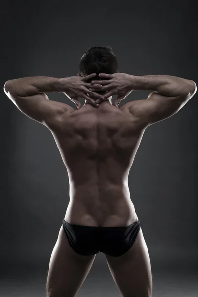 Stilig muskulös bodybuilder poserar på grå bakgrund. Låg nyckel studio skott — Stockfoto