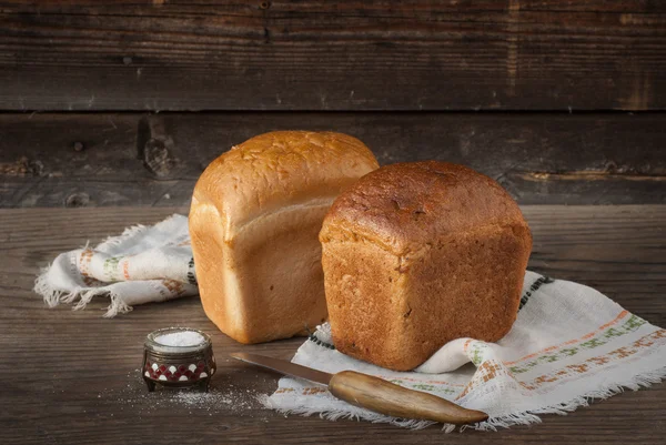 Due pani di pane, coltello, sale sdraiato su una superficie di legno — Foto Stock