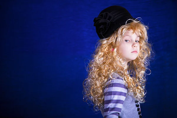 Retrato de una niña con un sombrero elegante sobre un fondo azul — Foto de Stock