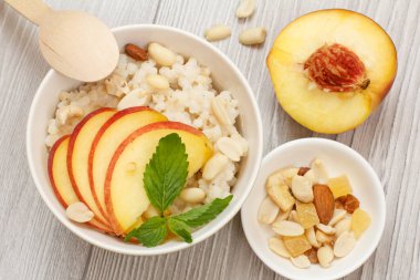 Şeftalili yulaf lapası, porselen kaselerde kaju fıstığı ve badem. Gri ahşap tahtalarda taze şeftali. Meyveli vegan glütensiz sorghum salatası.