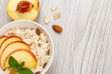 Şeftalili yulaf lapası, fındıklı kaju fıstığı ve porselen kasede badem. Gri ahşap tahtada taze şeftali. Meyveli vegan glütensiz sorghum salatası.