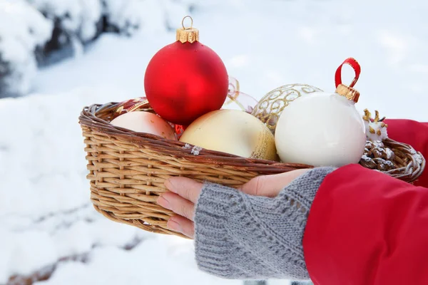 Woman is holding a wicker basket with christmas balls in winter city park with snow. Christmas or New year's composition.