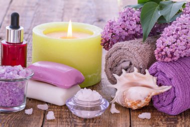Sabun, aromatik yağlı kırmızı şişe, yanan mum, deniz tuzu, deniz kabuğu, leylak çiçekleri ve tahta tahtalardaki banyo prosedürleri için havlular. Spa ürünleri ve aksesuarları