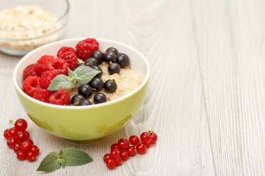 Nane yapraklarıyla süslenmiş frenk üzümü ve ahududu ile porselen kasede yulaf lapası. Arka planda yulaf lapası olan cam kaseler. Böğürtlenlere odaklan