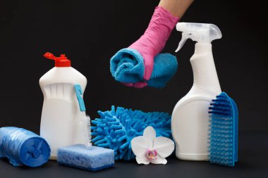 Azot eldivenli kadın eller, siyah arka planda temizlik seti olan plastik yıkama sıvısı şişelerinin yanında bir orkide çiçeği tutuyor. Yıkama ve temizleme seti.