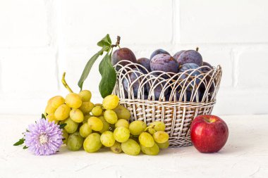 Hasır sepetin içinde olgun erikler ve paskalya çiçekli olgun beyaz üzümler topladım. Beyaz arka planda bir elma. Sadece meyve topladım..