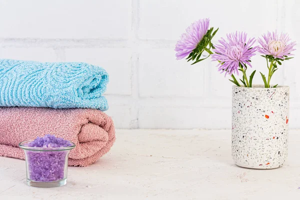 Can with sea salt, towels and flowers of asters on a white background. Woman cosmetics and wash accessories.