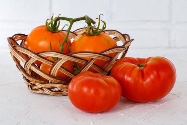 Yakın plan kırmızı ve sarı domatesler ve beyaz desenli arka planda hasır bir sepet. Vejetaryen yiyecekler için gerekli malzemeler.