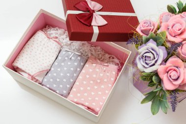 Beyaz arka planda suni çiçekler olan bir kutuda farklı renklerde katlanmış pamuk külotlar. Kadın iç çamaşırı seti. Üst görünüm.