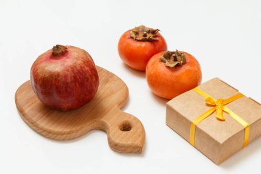 Olgun nar ve hurma meyveleriyle ahşap kesme tahtası ve beyaz arka planda hediye kutusu. Organik meyveler.