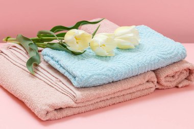 Pembe arka planda üç lale olan yumuşak havlu yığını..